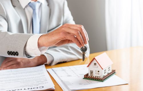 person-holding-house-keys-toy-model-house-desk_23-2148301737