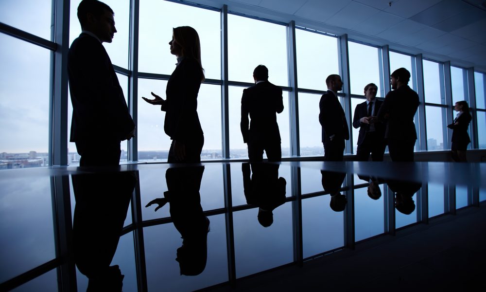 Group of colleagues standing against window in office and speaking